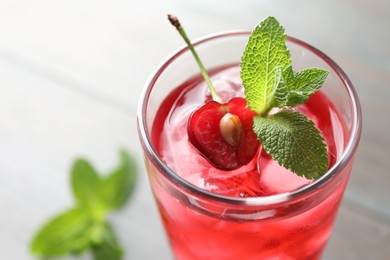 Photo of Tasty cherry soda water with ice cubes, berry and mint in glass on light table, closeup