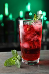 Photo of Tasty cherry soda water with ice cubes, berry and mint in glass on wooden table against blurred green background, closeup