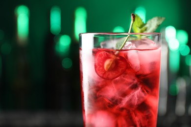 Photo of Tasty cherry soda water with ice cubes, berry and mint in glass on blurred green background, closeup