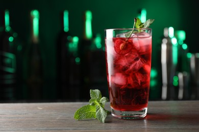 Photo of Tasty cherry soda water with ice cubes, berry and mint in glass on wooden table against blurred green background, closeup. Space for text