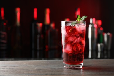 Photo of Tasty cherry soda water with ice cubes, berry and mint in glass on wooden table against blurred background, space for text