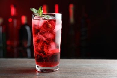 Photo of Tasty cherry soda water with ice cubes, berry and mint in glass on wooden table against blurred background