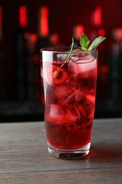Photo of Tasty cherry soda water with ice cubes, berry and mint in glass on wooden table against blurred background, closeup