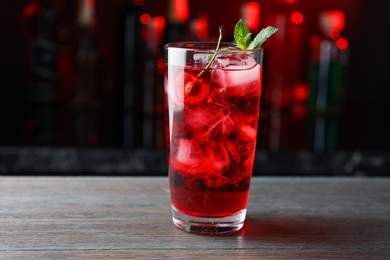 Photo of Tasty cherry soda water with ice cubes, berry and mint in glass on wooden table against blurred background, closeup