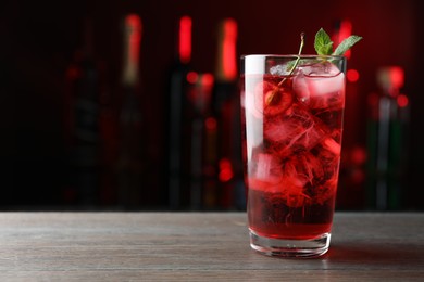 Photo of Tasty cherry soda water with ice cubes, berry and mint in glass on wooden table against blurred background, closeup. Space for text