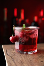 Photo of Tasty cherry soda water with ice cubes, berries and mint in glass on wooden table against blurred background, closeup