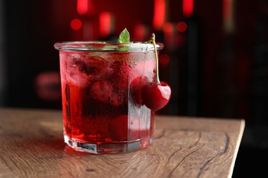Photo of Tasty cherry soda water with ice cubes, berries and mint in glass on wooden table against blurred background, closeup