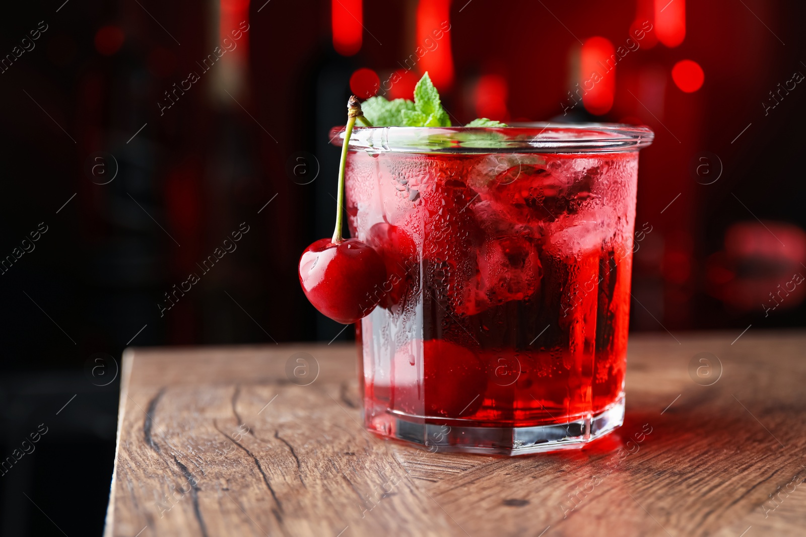 Tasty cherry soda water with ice cubes, berries and mint in glass on wooden table against blurred background, closeup. Space for text Photo of Tasty cherry soda water with ice cubes, berries and mint in glass on wooden table against blurred background, closeup. Space for text