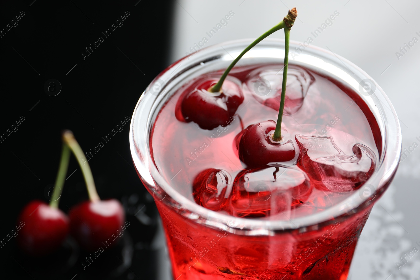 Tasty cherry soda water with ice cubes and berries in glass on color table, closeup Photo of Tasty cherry soda water with ice cubes and berries in glass on color table, closeup