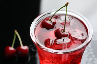 Photo of Tasty cherry soda water with ice cubes and berries in glass on color table, closeup