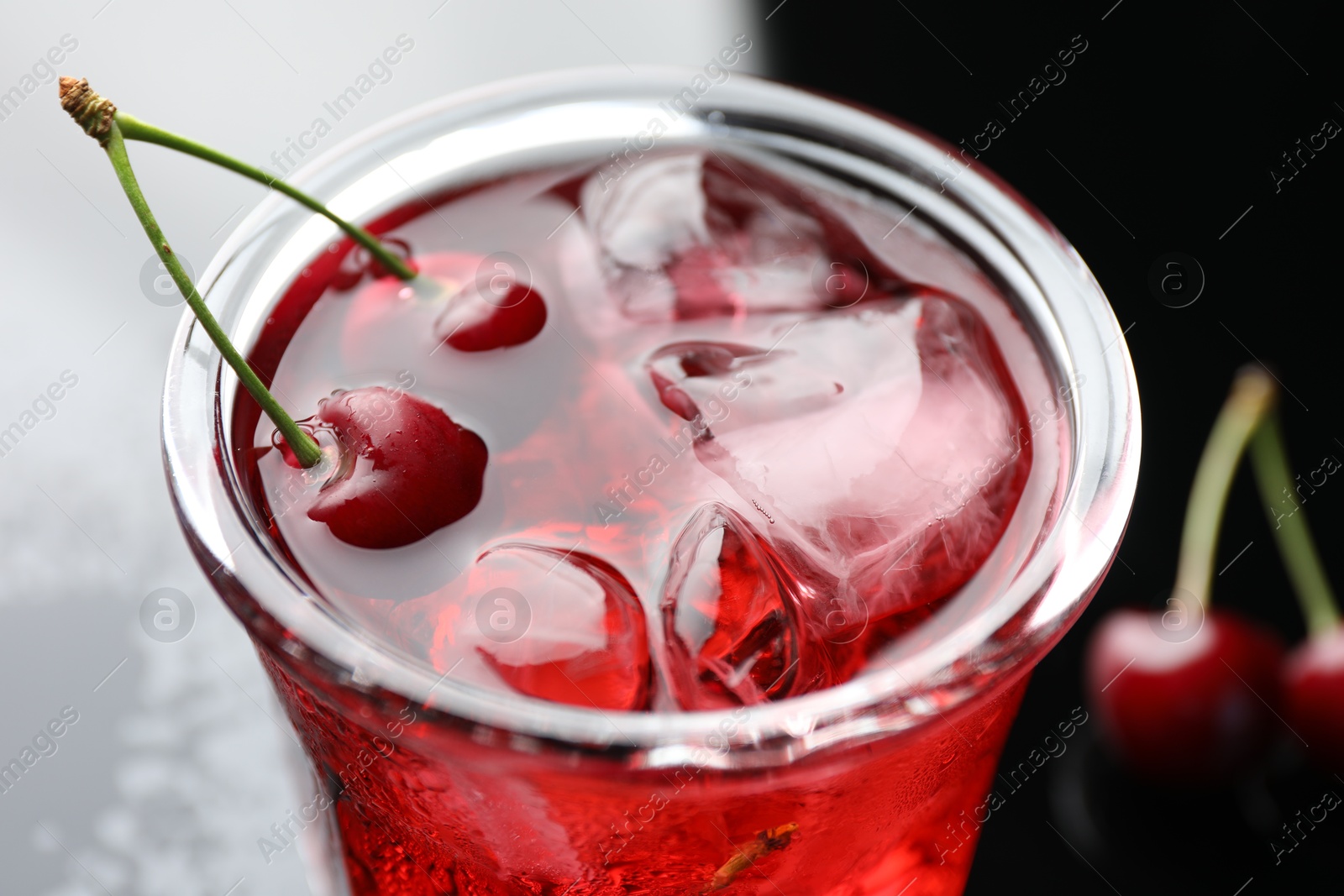 Tasty cherry soda water with ice cubes and berries in glass on color table, closeup Photo of Tasty cherry soda water with ice cubes and berries in glass on color table, closeup