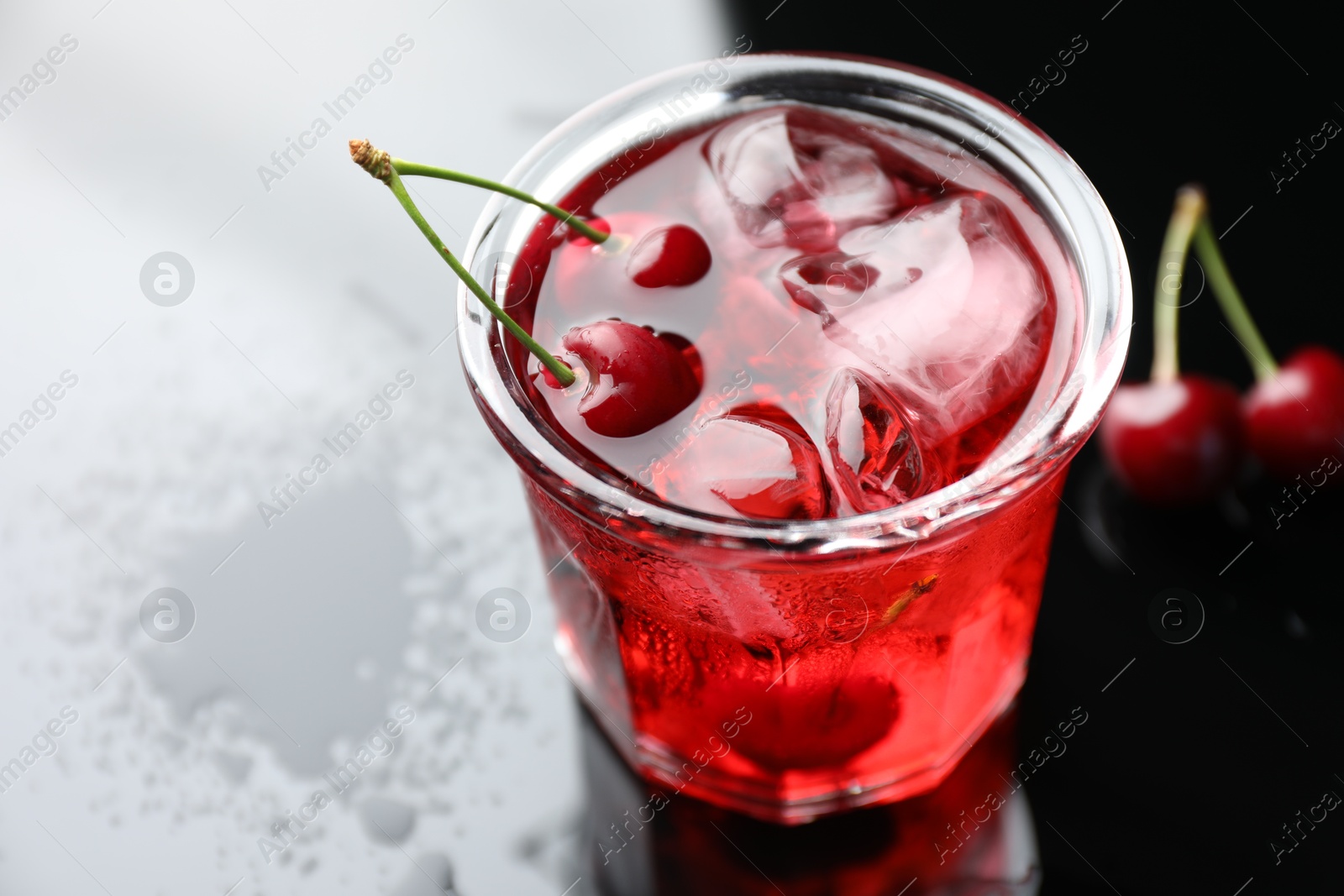 Tasty cherry soda water with ice cubes and berries in glass on color table, closeup Photo of Tasty cherry soda water with ice cubes and berries in glass on color table, closeup