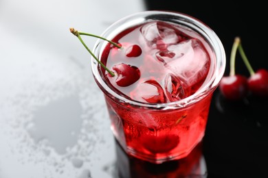 Photo of Tasty cherry soda water with ice cubes and berries in glass on color table, closeup