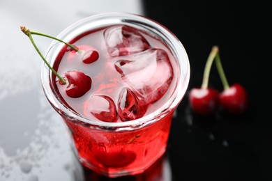 Photo of Tasty cherry soda water with ice cubes and berries in glass on color table, closeup