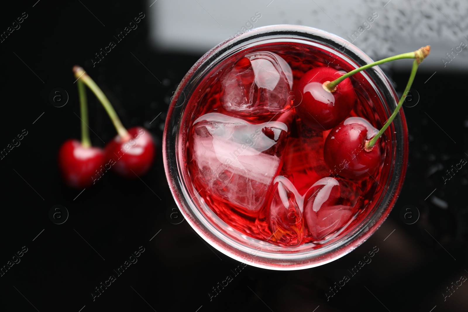 Tasty cherry soda water with ice cubes and berries in glass on dark table, top view Photo of Tasty cherry soda water with ice cubes and berries in glass on dark table, top view
