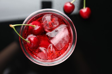 Photo of Tasty cherry soda water with ice cubes and berries in glass on dark table, top view