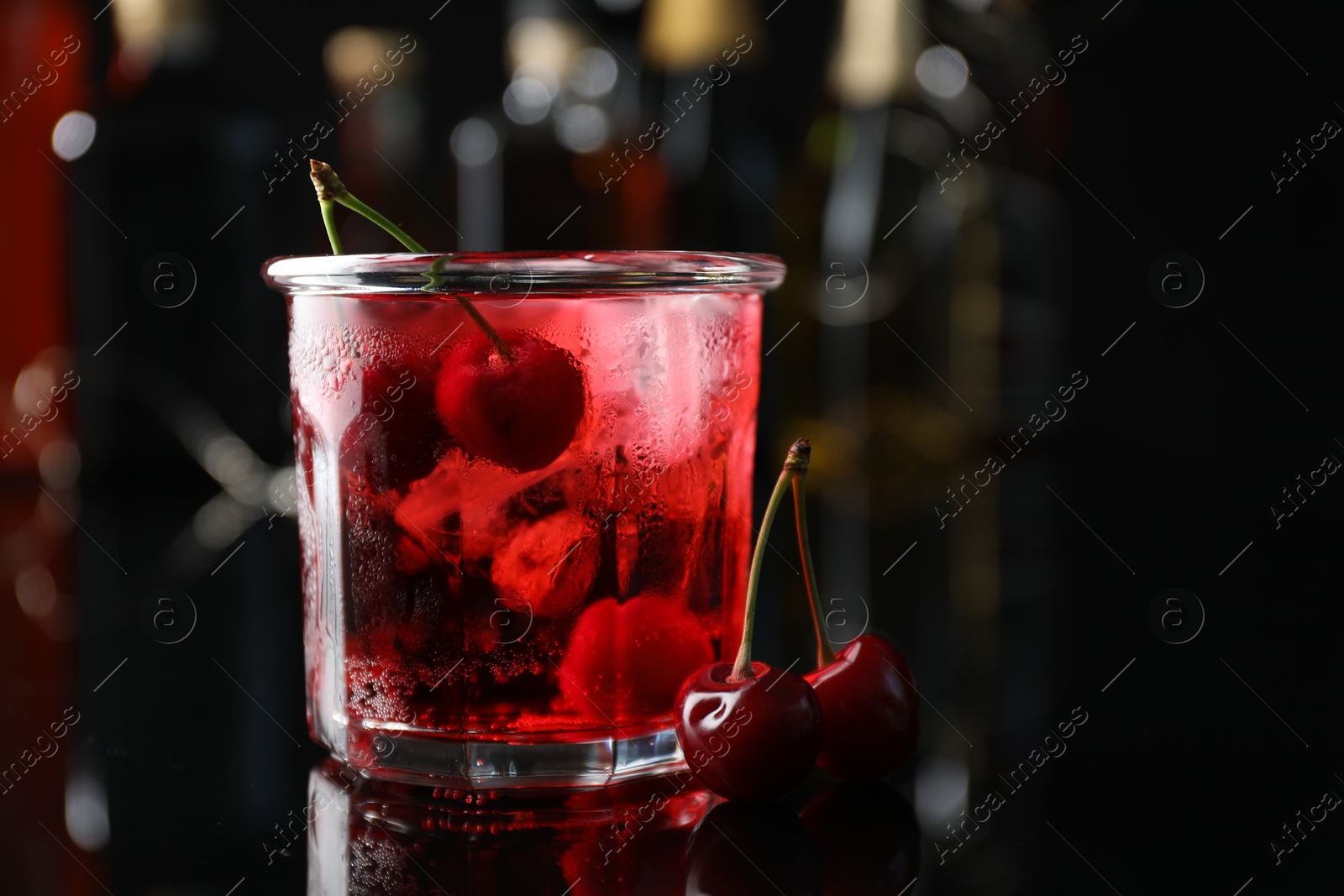 Tasty cherry soda water with ice cubes and berries in glass on mirror table against blurred background, closeup Photo of Tasty cherry soda water with ice cubes and berries in glass on mirror table against blurred background, closeup
