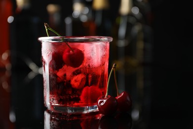 Photo of Tasty cherry soda water with ice cubes and berries in glass on mirror table against blurred background, closeup