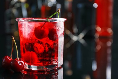 Photo of Tasty cherry soda water with ice cubes and berries in glass on mirror table against blurred background, closeup