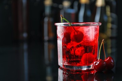 Photo of Tasty cherry soda water with ice cubes and berries in glass on mirror table against blurred background, closeup. Space for text