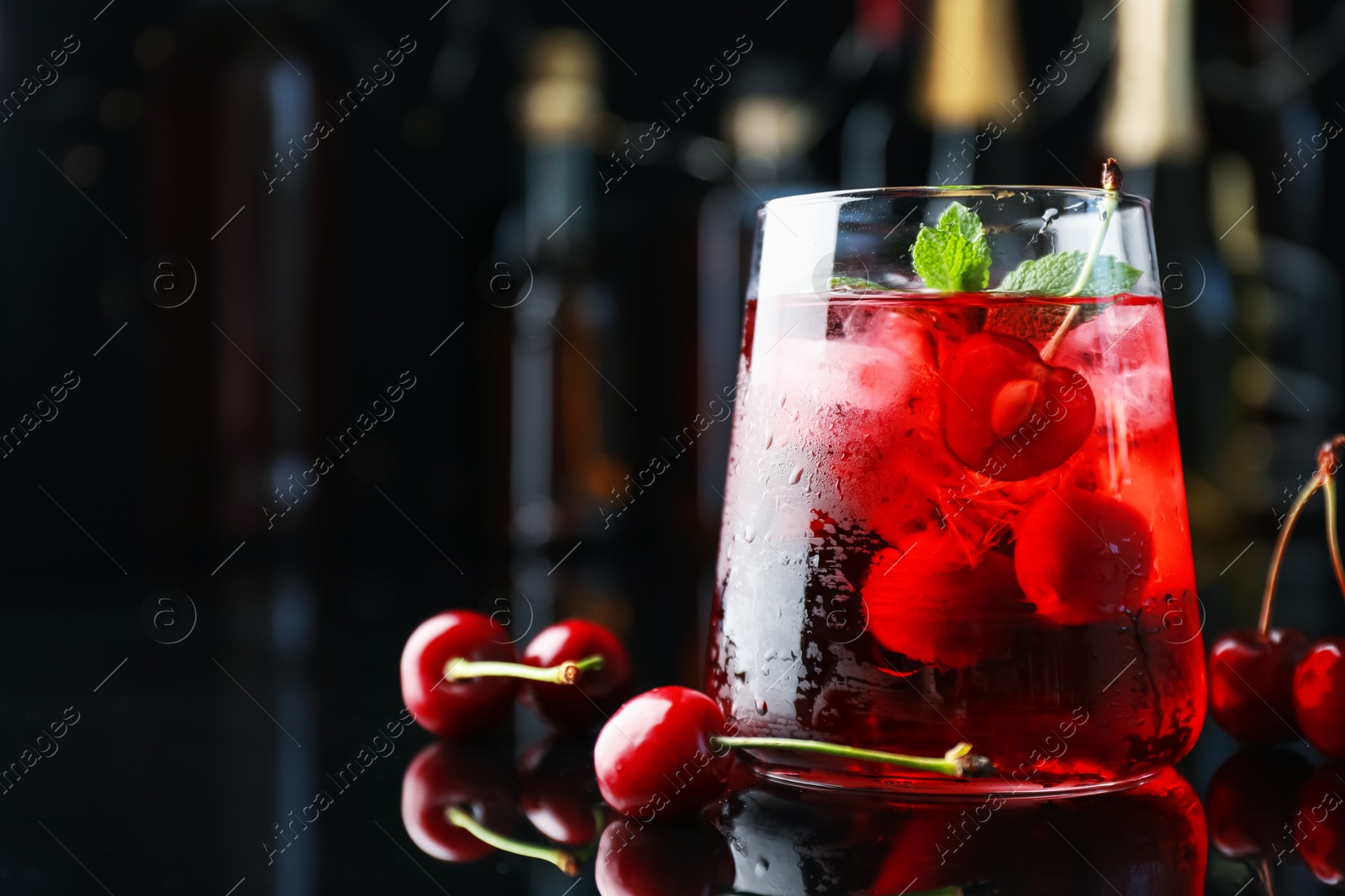 Tasty cherry soda water with ice cubes, berries and mint in glass on mirror table against blurred background, closeup. Space for text Photo of Tasty cherry soda water with ice cubes, berries and mint in glass on mirror table against blurred background, closeup. Space for text
