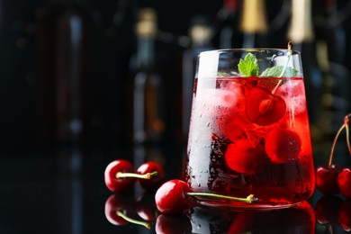 Photo of Tasty cherry soda water with ice cubes, berries and mint in glass on mirror table against blurred background, closeup. Space for text
