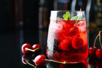 Photo of Tasty cherry soda water with ice cubes, berries and mint in glass on mirror table against blurred background, closeup. Space for text