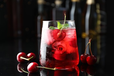 Photo of Tasty cherry soda water with ice cubes, berries and mint in glass on mirror table against blurred background, closeup