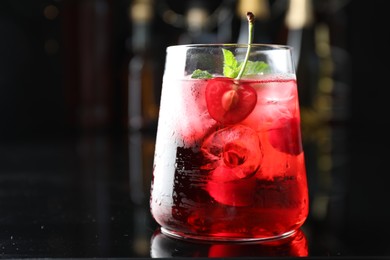 Photo of Tasty cherry soda water with ice cubes, berry and mint in glass on mirror table against blurred background, closeup. Space for text