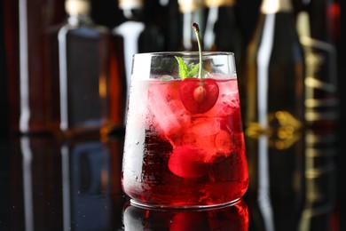 Photo of Tasty cherry soda water with ice cubes, berry and mint in glass on mirror table against blurred background, closeup
