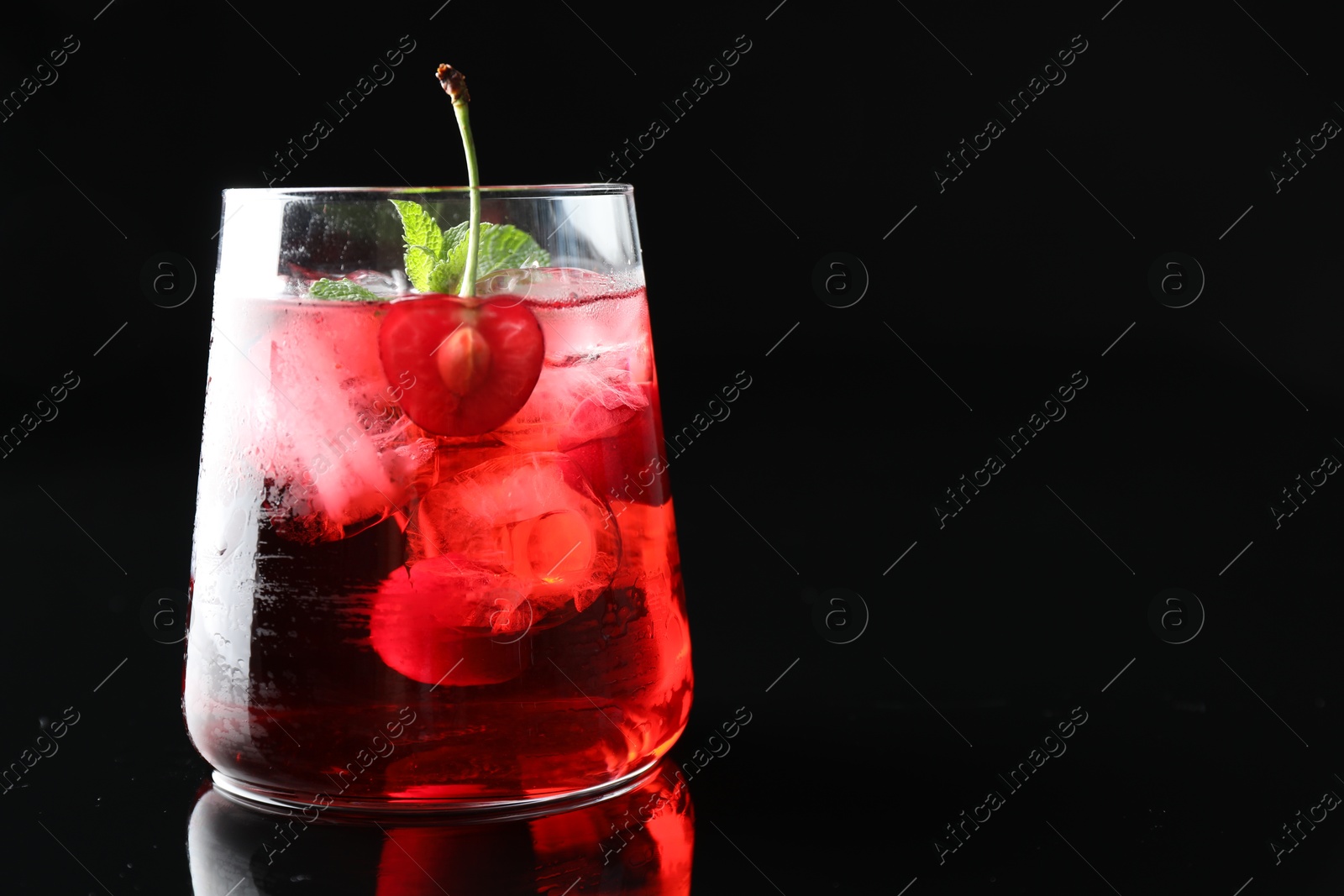 Tasty cherry soda water with ice cubes, berry and mint in glass on mirror table against black background, closeup. Space for text Photo of Tasty cherry soda water with ice cubes, berry and mint in glass on mirror table against black background, closeup. Space for text