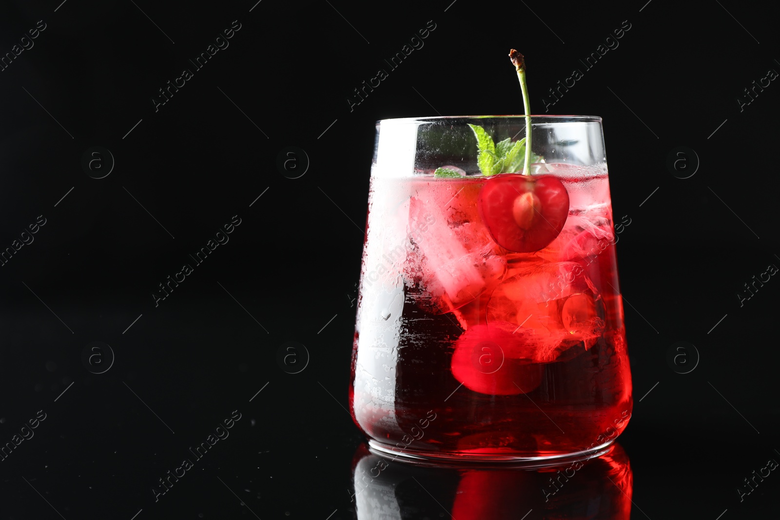 Tasty cherry soda water with ice cubes, berry and mint in glass on mirror table against black background, closeup. Space for text Photo of Tasty cherry soda water with ice cubes, berry and mint in glass on mirror table against black background, closeup. Space for text