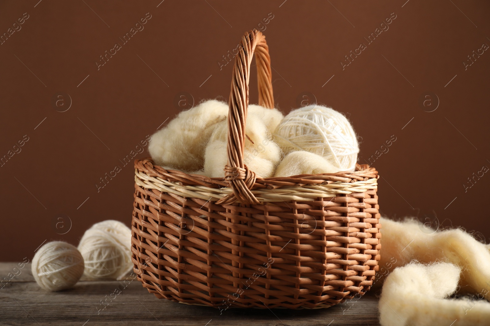 Felting wool and knitting yarn in basket on wooden table Photo of Felting wool and knitting yarn in basket on wooden table