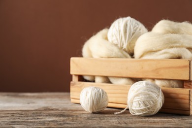 Photo of Felting wool and knitting yarn on wooden table, closeup. Space for text