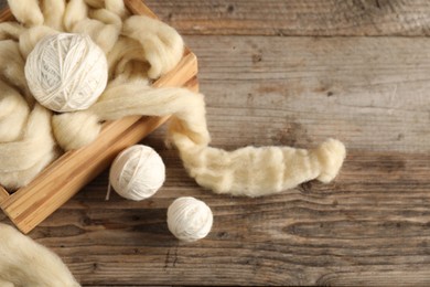 Photo of Felting wool and knitting yarn on wooden table, closeup. Space for text