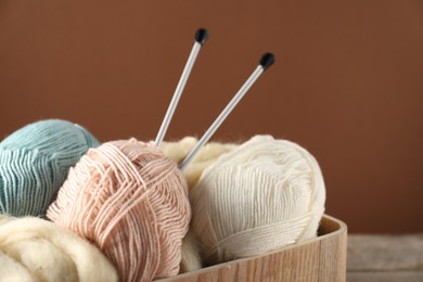 Photo of Felting wool and knitting yarn with needles on brown background, closeup