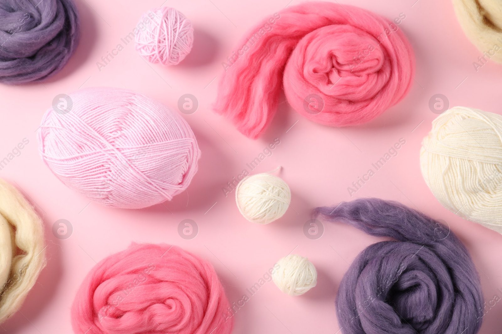 Felting wool and knitting yarn on pink background, flat lay Photo of Felting wool and knitting yarn on pink background, flat lay