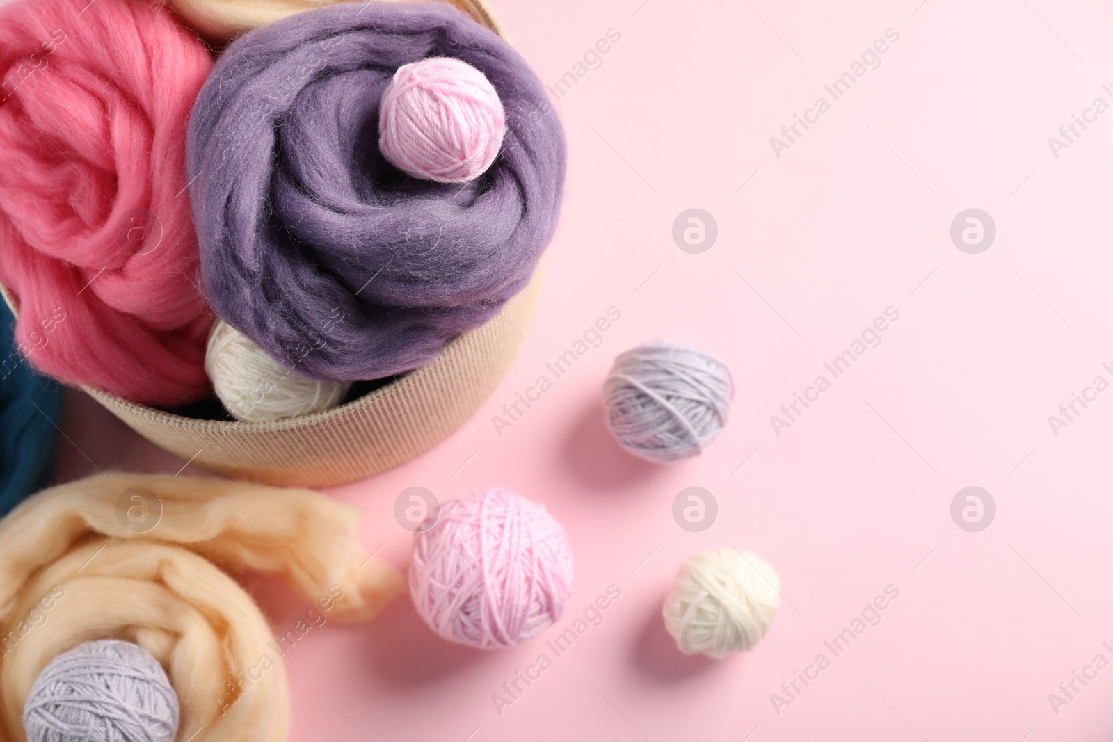 Felting wool and knitting yarn on pink background, above view. Space for text Photo of Felting wool and knitting yarn on pink background, above view. Space for text