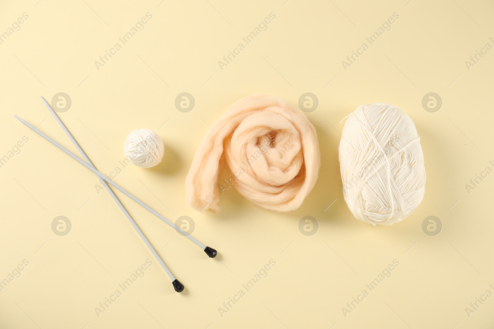 Felting wool and knitting yarn with needles on beige background, flat lay Photo of Felting wool and knitting yarn with needles on beige background, flat lay