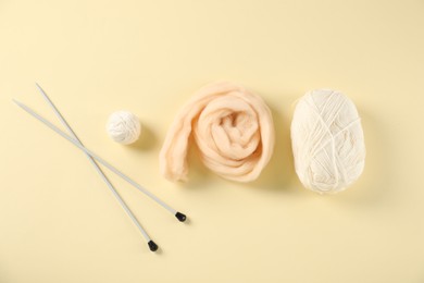 Photo of Felting wool and knitting yarn with needles on beige background, flat lay
