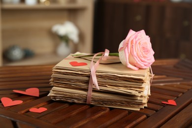 Photo of Stack of love letters, rose flower and paper hearts on wooden table indoors, closeup