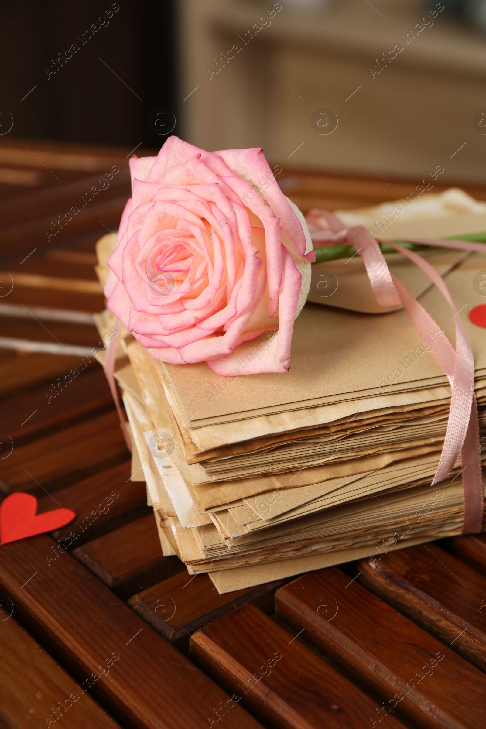 Photo of Stack of love letters, rose flower and paper heart on wooden table indoors, closeup