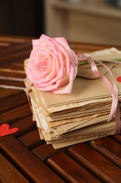 Photo of Stack of love letters, rose flower and paper heart on wooden table indoors, closeup