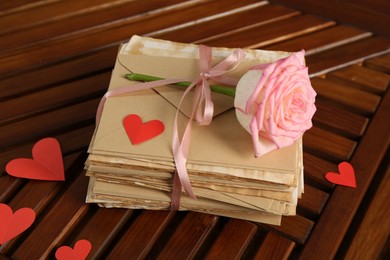 Photo of Stack of love letters, rose flower and paper hearts on wooden table indoors, above view