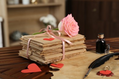 Photo of Stack of love letters, parchment sheet, ink, quill, rose flower and red hearts on wooden table indoors, closeup