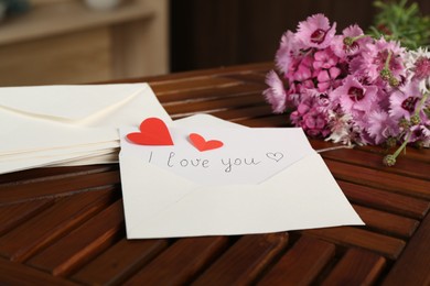 Photo of Card with phrase I Love You, letters, red hearts and flowers on wooden table indoors, closeup