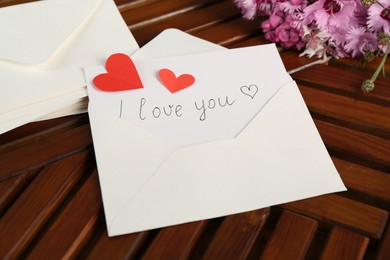 Photo of Card with phrase I Love You, letters, red hearts and flowers on wooden table, above view