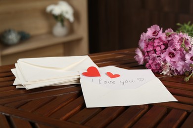Photo of Card with phrase I Love You, letters, red hearts and flowers on wooden table indoors, closeup
