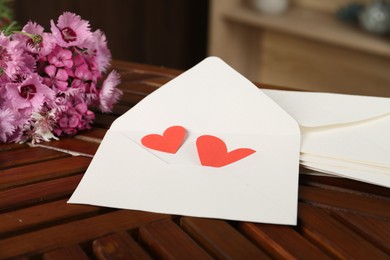 Photo of Love letters, red hearts and flowers on wooden table indoors, closeup