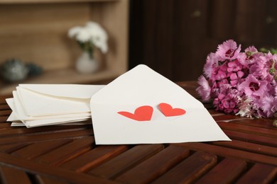 Photo of Love letters, red hearts and flowers on wooden table indoors, closeup